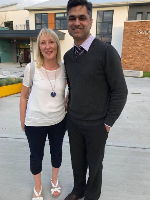 A man and a woman smiling together outdoors in front of a modern building with brick and glass.