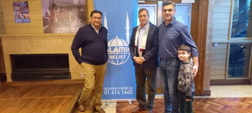 A group posing in front of an Islamic Relief banner at a community venue with wood panelling.